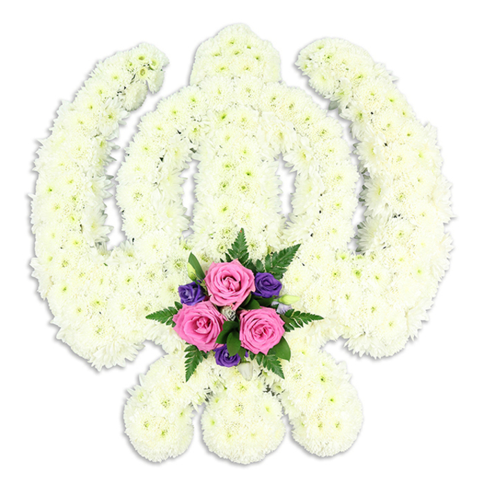 A beautifully detailed Sikh Khanda floral tribute fills the frame, photographed head-on against a neutral white background so that all attention falls on the symbolic design. The entire Khanda shape is rendered from countless small white chrysanthemum florets, carefully positioned to outline the central sword, the surrounding chakkar ring, and the two balanced kirpans that sweep upward on each side. Each chrysanthemum head is plump and fresh, with layered petals overlapping to form a thick, padded surface that feels gentle to the eye, mirroring the quiet compassion many families seek when arranging funeral flowers in Abbey Wood. The uniform white blooms have just a touch of creamy softness, adding dimension as light glides over their rounded forms. At the lowest point of the design, where the sword blades visually come together, a vivid accent of colour provides contrast and emotional warmth. Three rich pink roses are gathered tightly in the centre, their petals unfurling in soft spirals, framed by several smaller deep purple blossoms that introduce a note of dignified depth. Fine, feathery fronds of dark green fern and other greenery emerge from behind this cluster, breaking the white surface and drawing the eye downwards like a focal point at the base of a memorial display near Bostall Woods. The background is completely uncluttered, and the lighting is gentle and even, revealing every petal and leaf without harsh glare. A faint shadow beneath the tribute gives a sense of weight and stability, as if it rests on a table ready for delivery to a gurdwara or family home in Abbey Wood. Crafted with reverence by Florist Abbey Wood, this Khanda arrangement offers a moving floral expression of Sikh faith, honour, and remembrance for funerals and memorial services throughout SE2 and nearby areas.