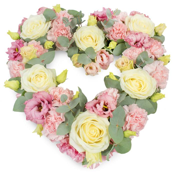 A tender, heart-shaped wreath in harmonising pastel shades is presented against a clean white background, which enhances the sense of purity and calm surrounding the arrangement. The heart is carefully defined, its outline and centre densely packed with flowers so that the form appears soft, full, and comforting. At focal points along the heart's curve, large cream and pale yellow roses emerge, their velvety petals unfurling from tight centres into generous, open blooms that convey warmth, dignity, and affection. Filling the spaces around these roses, clusters of light pink carnations create a textured base, their finely fringed petals layered on top of one another to produce a gentle, ruffled surface reminiscent of delicate lace. Nestled among them, deeper pink and mauve lisianthus blossoms provide accents of richer colour, some blooms cupped, others more open, introducing a sense of movement and shadow that brings the wreath to life. Threading calmly through the arrangement, sprigs of silvery eucalyptus add a muted green note; their round, soft-edged leaves follow the contours of the heart, offering subtle contrast and the idea of a cool woodland breeze like those felt in Abbey Wood's leafy parkland. Small, yellow-green buds appear at intervals, suggesting newly opened flowers and meticulous conditioning suitable for same-day sympathy flower delivery across Abbey Wood and the surrounding neighbourhoods. The design is balanced, luxurious, and deeply expressive, making it an ideal tribute for funeral services, church ceremonies, or graveside remembrances, where the heart shape serves as a clear emblem of love, gratitude, and cherished memories that endure beyond the day of farewell.